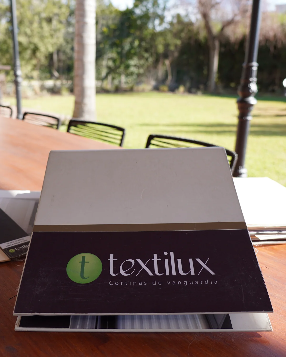 El muestrario de telas de Textilux sobre la mesa, a la luz del jardín